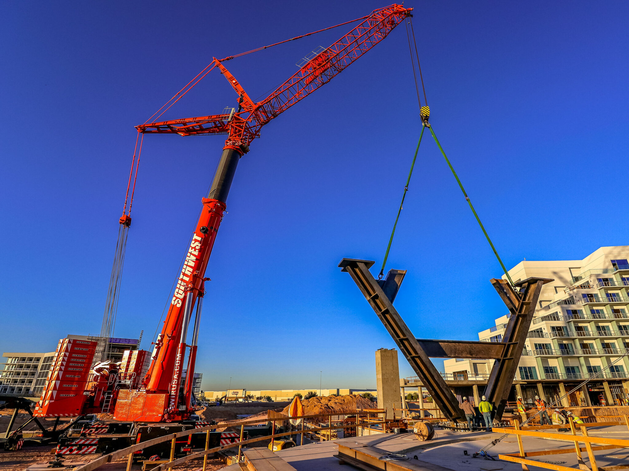 Large red construction crane lifting a steel beam at a building site.