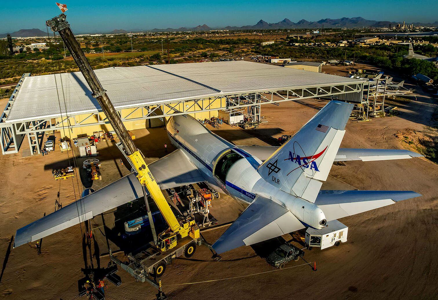 NASA aircraft undergoing maintenance outdoors with cranes and technicians.