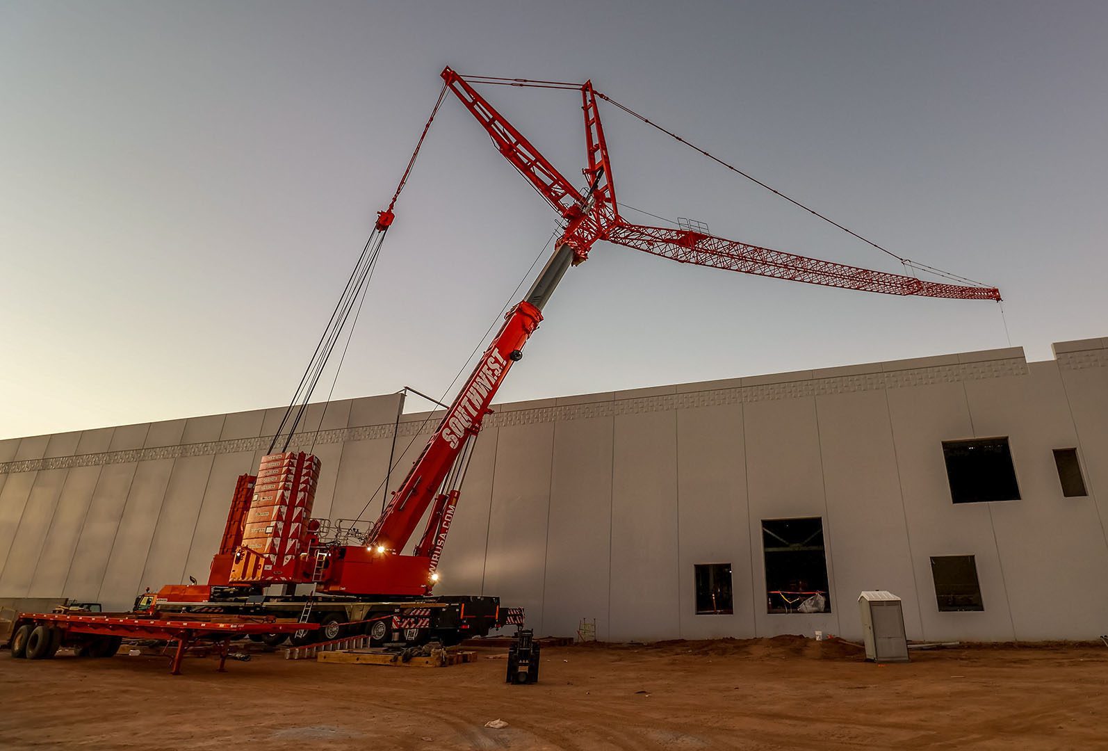 A large red construction crane at a building site during sunset.