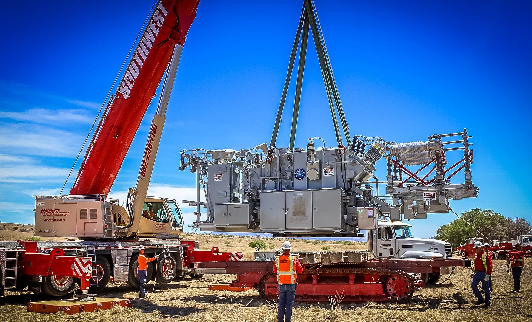 Construction workers lift a large transformer at a power site.