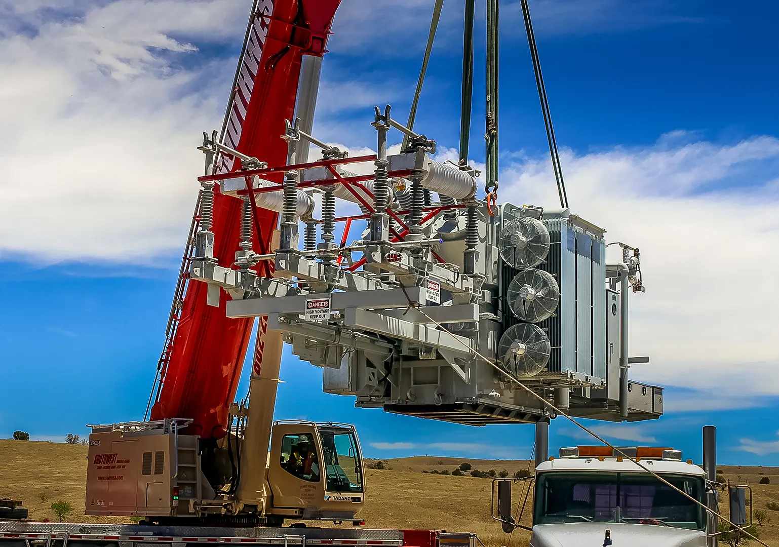 A large transformer being lifted by a crane at a construction site.